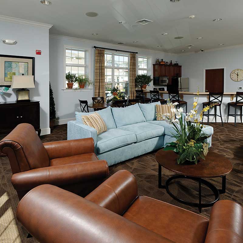 Clubhouse with 3 couches, multiple chairs with a table and island bar and plants around the room.