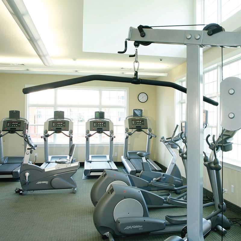 Fitness center with multiple large windows and various workout equipment.