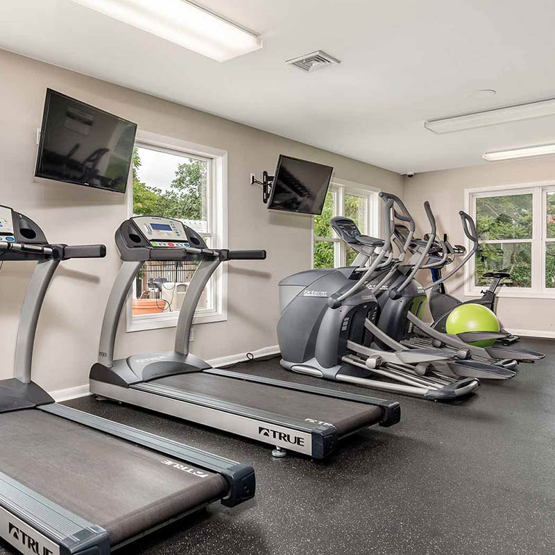 Fitness center with tvs, windows, and various workout equipments.