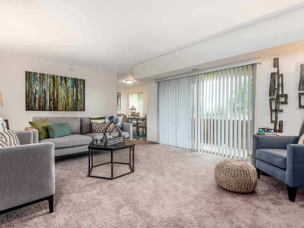 Carpeted living room with chairs and a sofa facing sliding window doors connected to the dining area