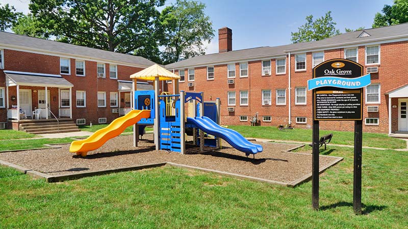 Playground on mulch with grass, walkways at Oak Grove apartments