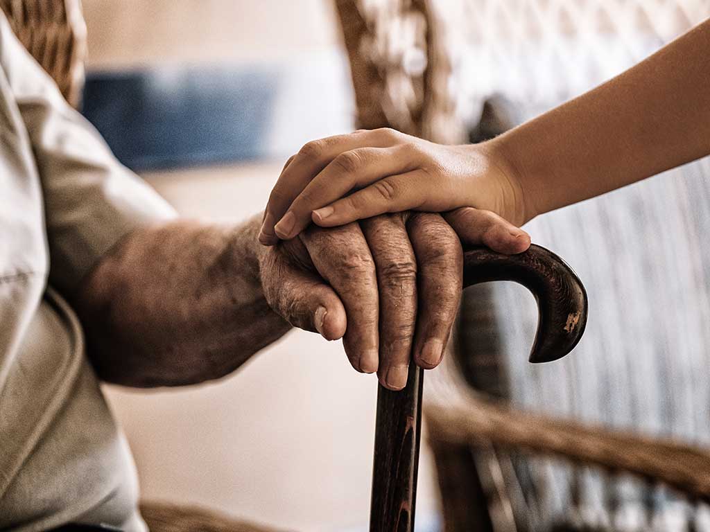 Young hand placed over older person's hand on a cane